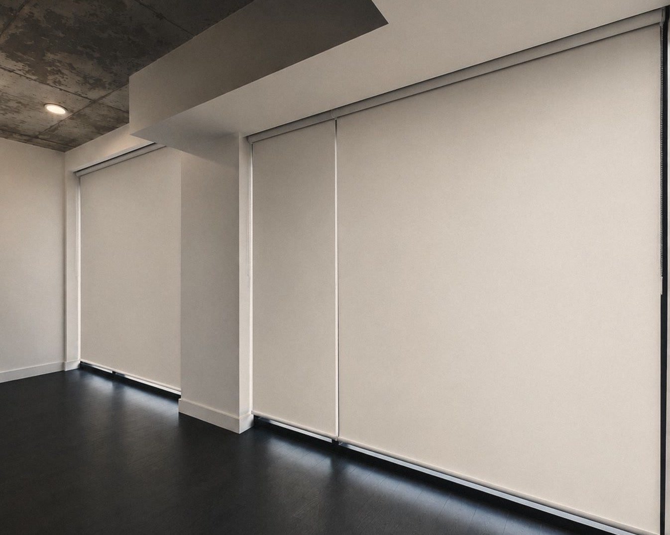 Une pièce avec des toiles enrouleuses descendues sur tout un mur de fenêtres.